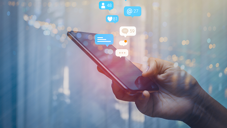 Person using a social media marketing concept on mobile phone with notification icons of like, message, comment and star above smartphone screen.