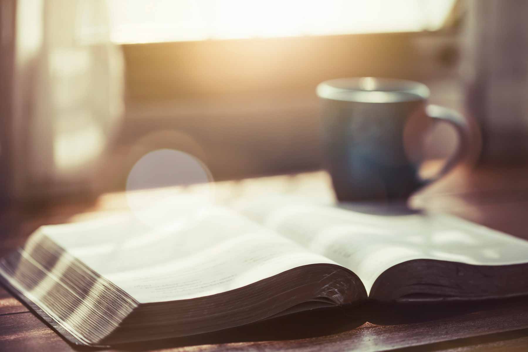 close up of open bible with a cup of coffee for morning devotion on wooden table with window light