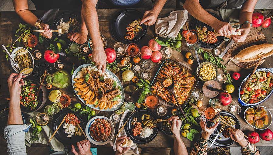 Flat-lay of family feasting with Turkish cuisine lamb chops, quince, bean, vegetable salad, babaganush, rice pilav, pumpkin dessert, lemonade over rustic table, top view. Middle East cuisine