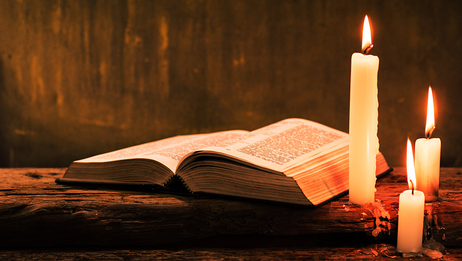 Bible and candle on a old oak wooden table.  Beautiful gold background.Religion concept.