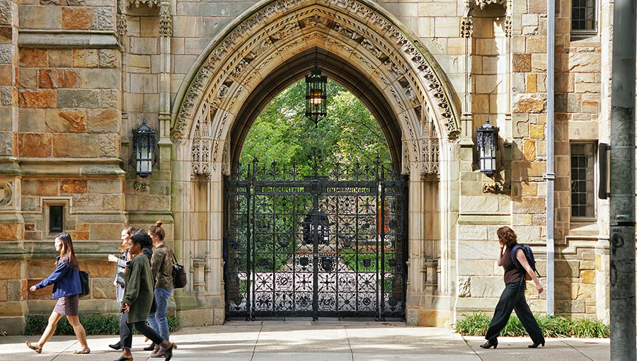 YALE UNIVERSITY, NEW HAVEN, CONNECTICUT, USA - OCTOBER 2017: A decorative stone archway at the entrance to a student college. An ornate metal gate is closed to prevent access. Green trees can be seen